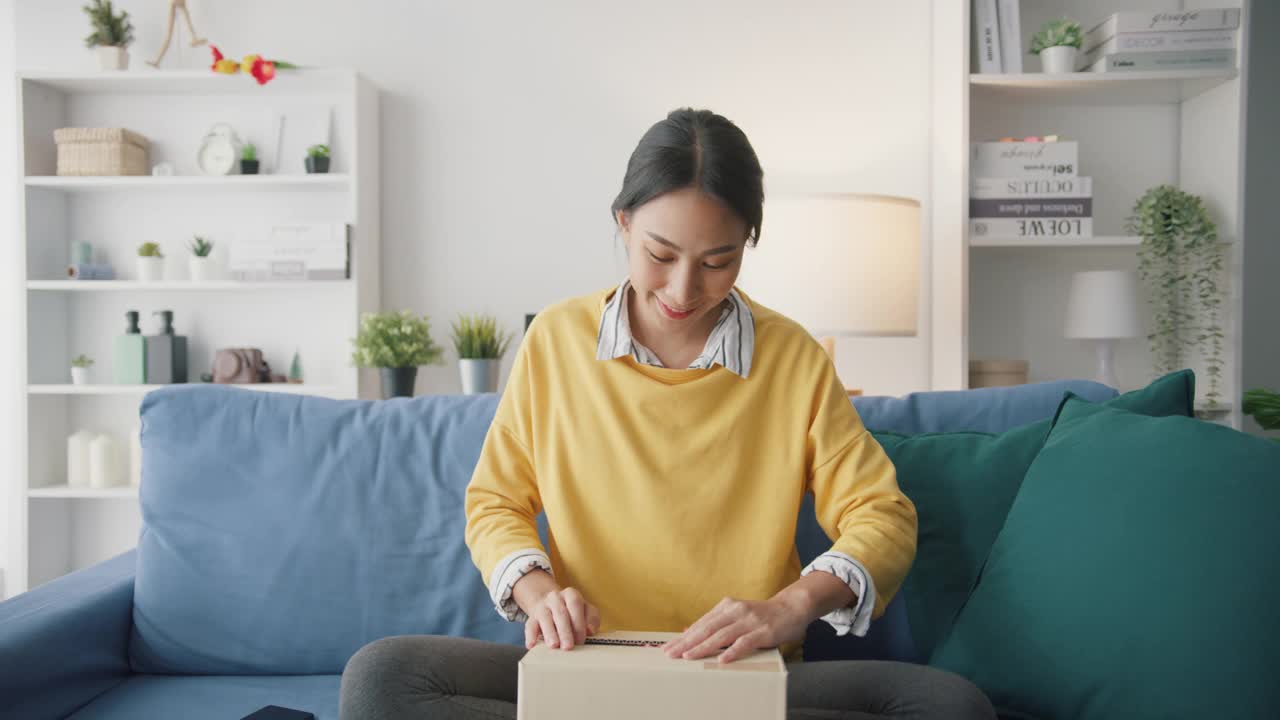 年轻女子在家中客厅沙发上打开纸箱收包裹。视频素材