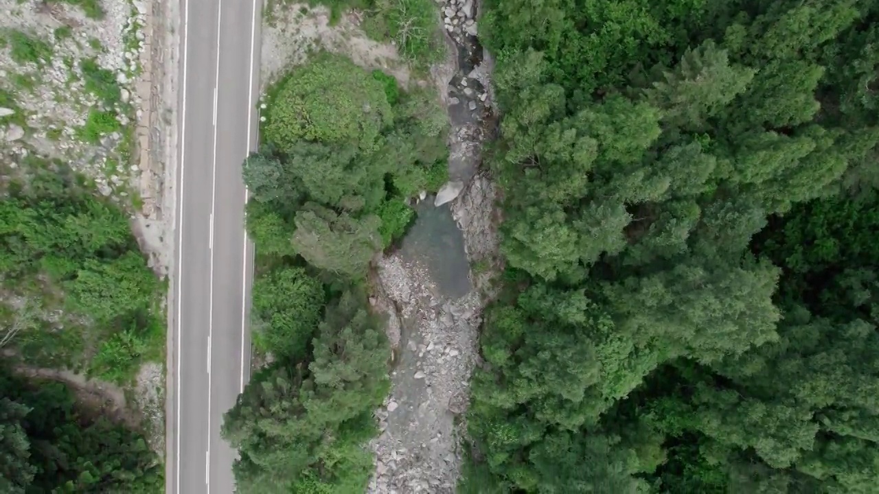 在高山峡谷中的柏油路。在它旁边，一条山间河流在树林间蜿蜒流过。视频素材