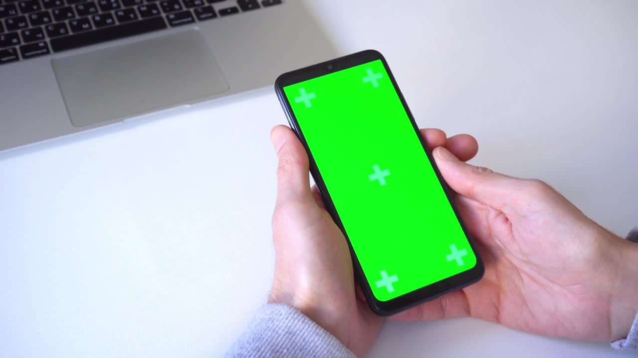 特写镜头。4 k。男子双手握住智能手机，按下手指，滚动绿色屏幕的色度键。点击应用程序图标，玩游戏，用手指滑动，写信息视频下载