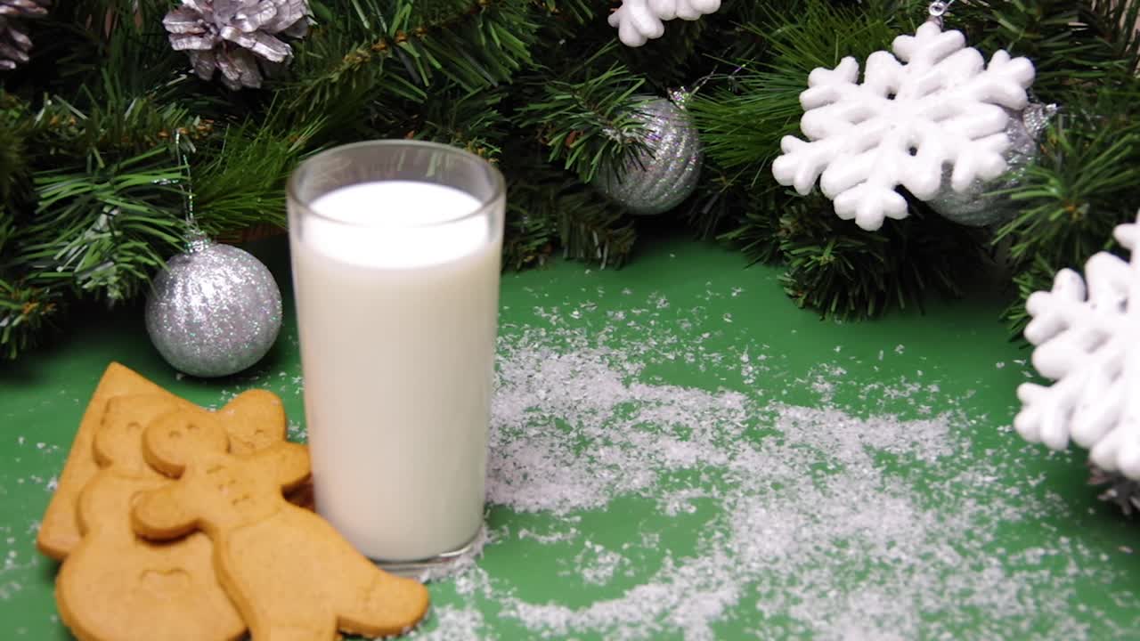 人造雪花飘落在圣诞饼干、一杯牛奶和圣诞装饰品上。给圣诞老人的圣诞礼物。全高清视频素材