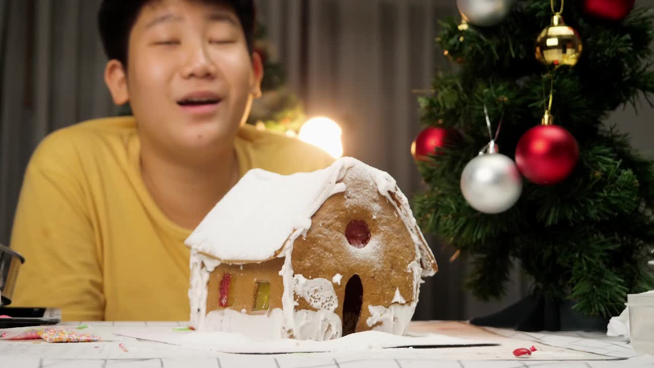 亚洲男孩看着DIY姜饼屋完成后，圣诞节庆祝生活方式的概念。视频素材