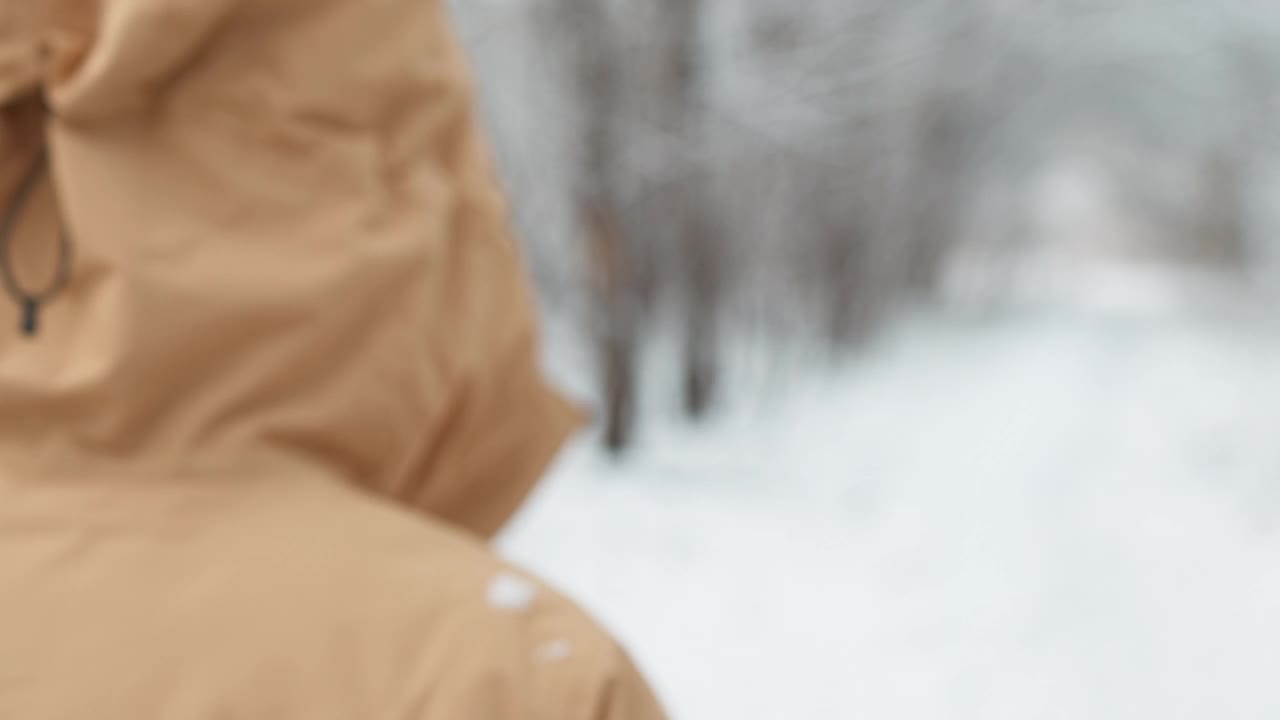 从离焦到离焦。成熟的女人穿着黄色的冬季夹克，头戴兜帽，走在雪地里的公园里。视频素材