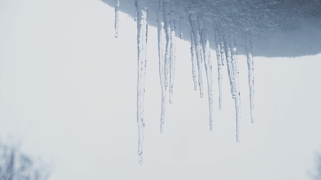 积雪覆盖的屋顶上悬挂着巨大的冰柱，它们正在慢慢融化。解冻，春天的到来，全球变暖的概念。视频素材