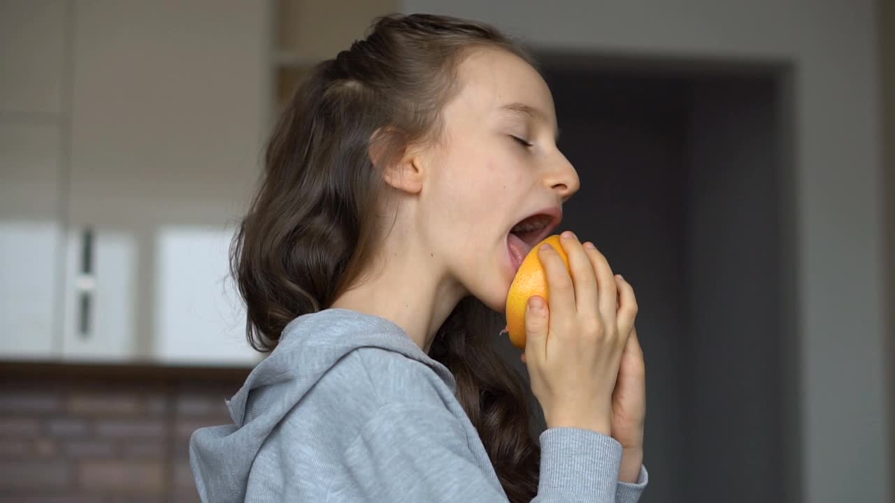 长头发的小女孩正在舔半个橘子。快乐童年，健康饮食视频素材