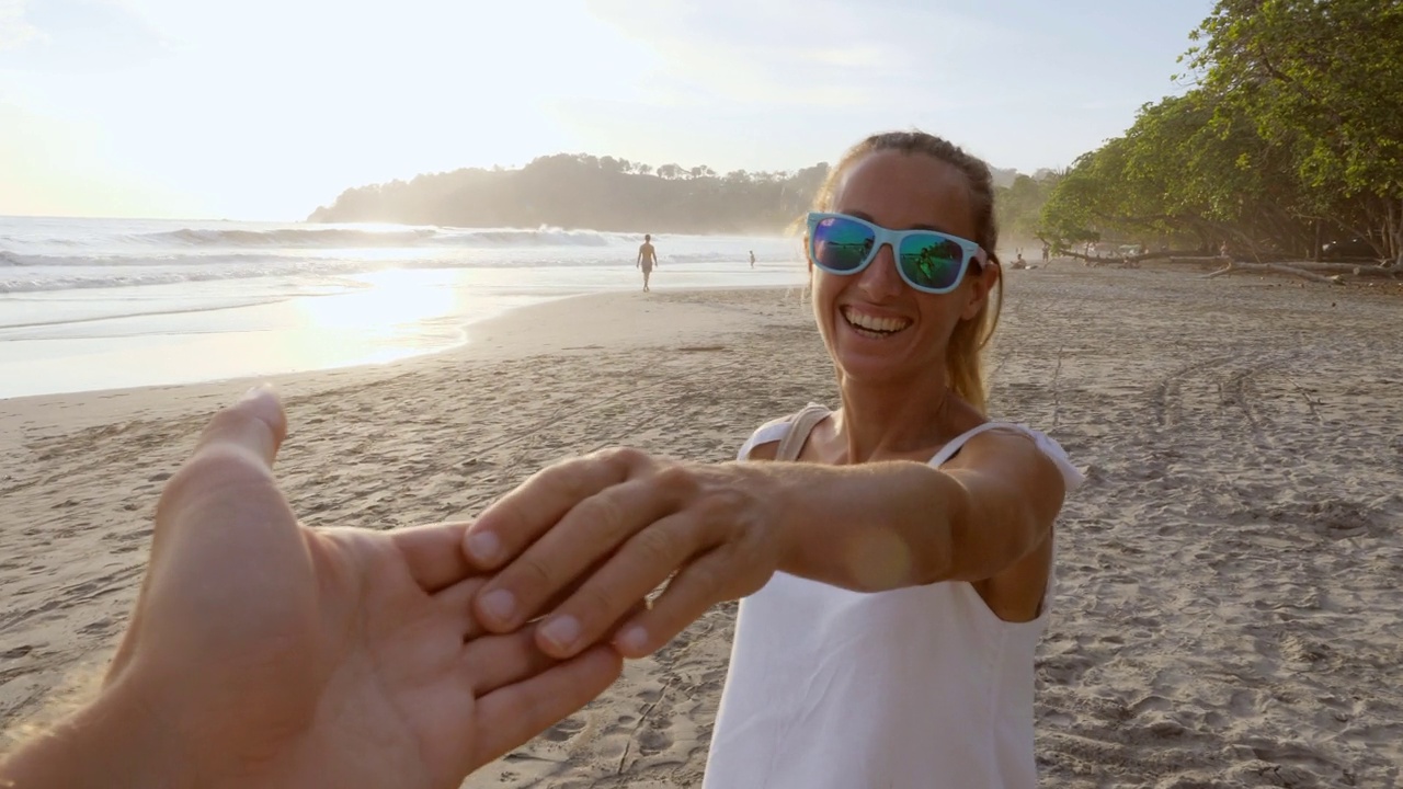 夫妇手牵手，女人引领的方式，热带海滩在日落享受假期。男人跟踪女友到异国他乡视频素材