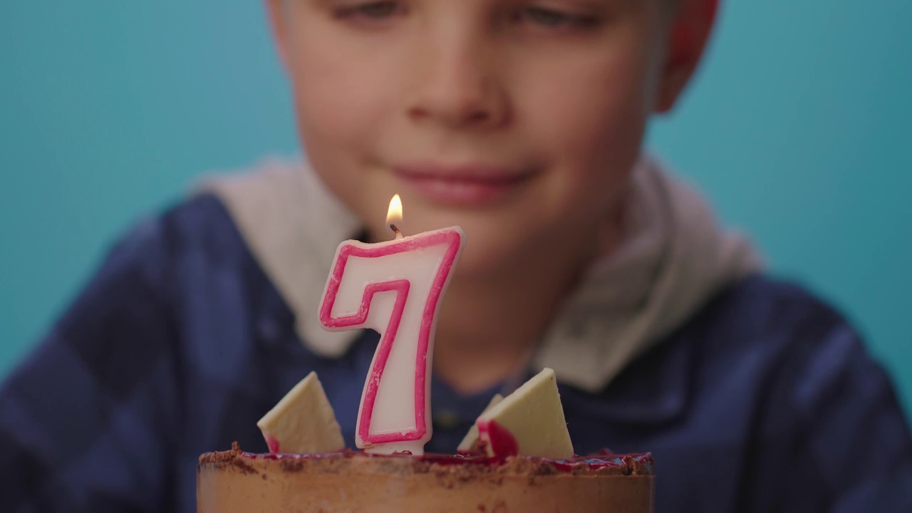 小男孩许了个愿，然后吹灭了7号蜡烛的慢镜头。一个七岁的男孩庆祝生日。快乐的7岁孩子。视频素材