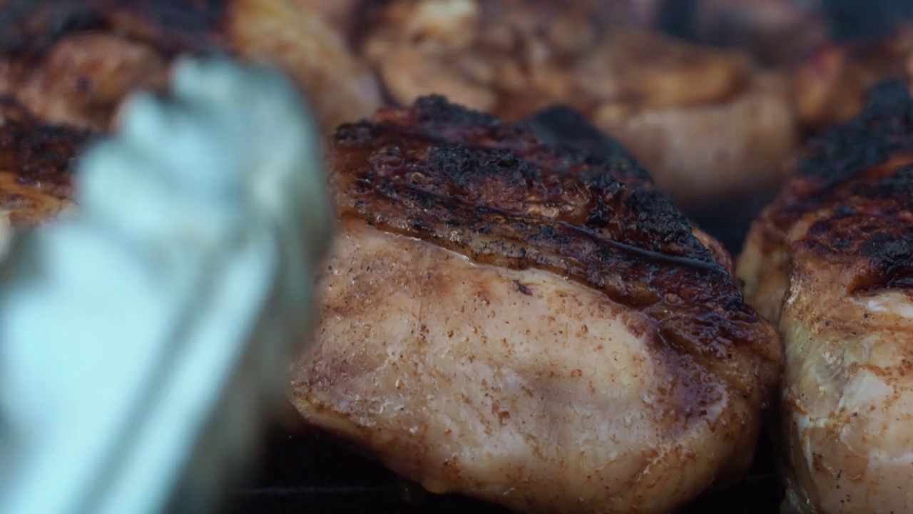 他用钳子把鸡大腿放在烤架上。一个男人的手。一大块鸡肉视频素材