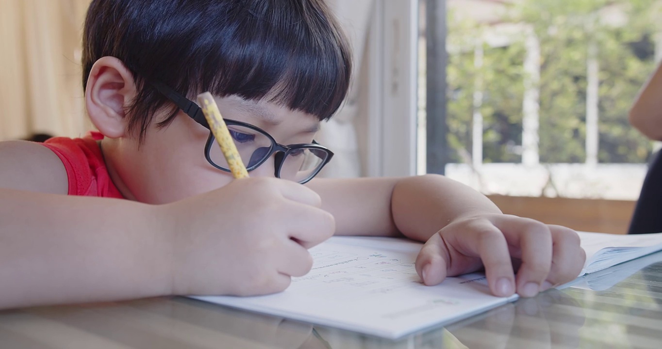 可爱聪明的亚洲小孩小孩在家里坐在书桌前学习，学生在作业本上写作业，教育理念视频素材