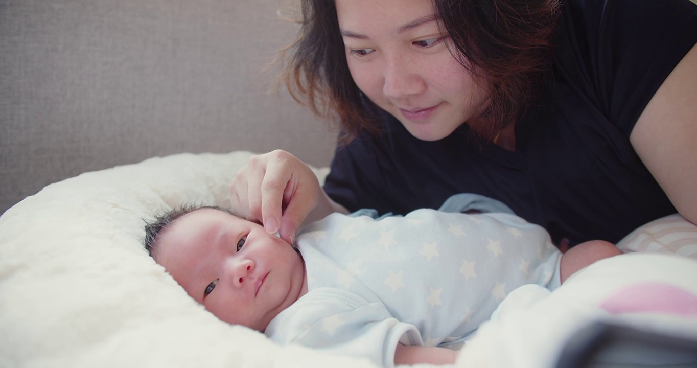 亚洲母亲与她漂亮的新生婴儿女婴在家中早上躺在床上玩耍，孩子，父母，童年，生活，母性，母亲的概念视频素材