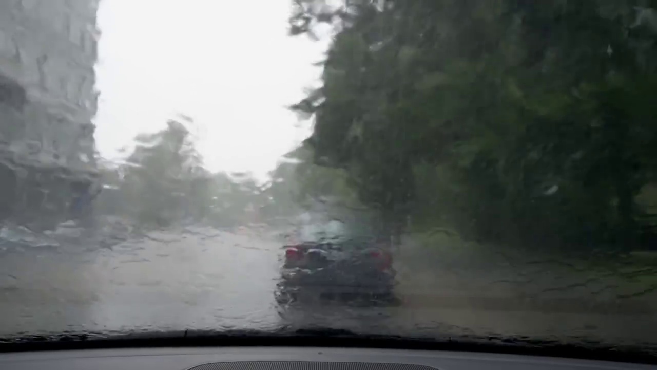 树木和街景透过雨点覆盖的汽车挡风玻璃。视频素材