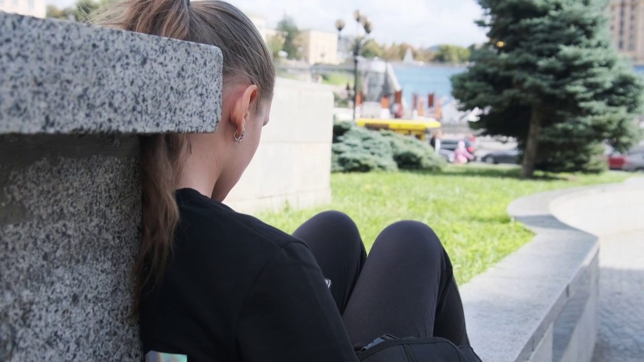 年轻女子坐在街道公园的栏杆上使用智能手机视频素材