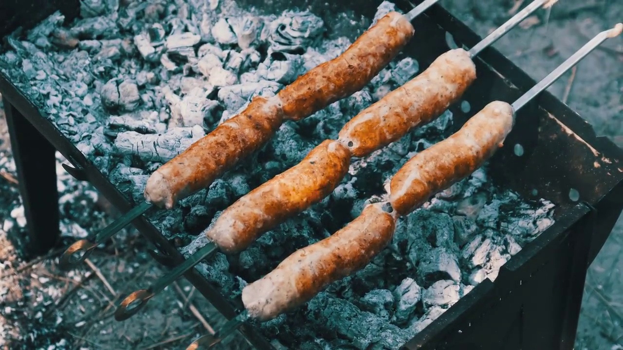 在烤肉串上的香肠是在户外便携式烤架上烤的，近距离，烧烤视频素材