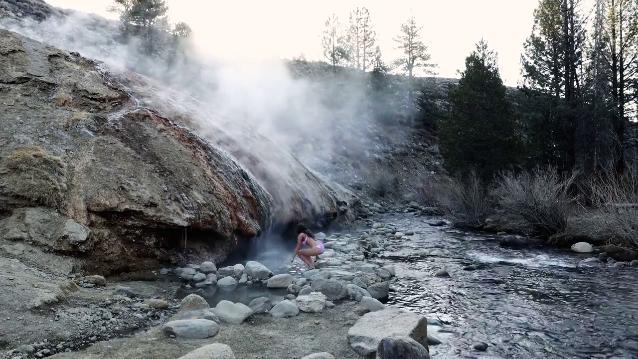 一名年轻女子在一个热带度假胜地，那里有温泉、瀑布和有热矿泉水的游泳池。慢动作镜头库存视频视频素材