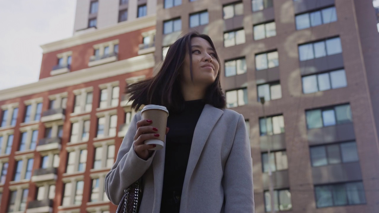 一个亚洲女商人的低角度肖像在现代城市的街道上喝咖啡视频素材