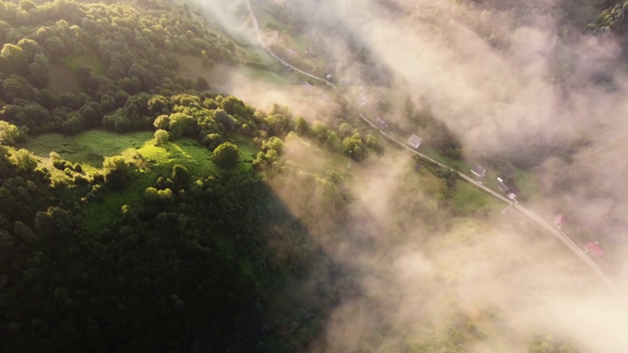 晨雾笼罩着山和河的草地，附近有一个小村庄，鸟瞰风景视频素材