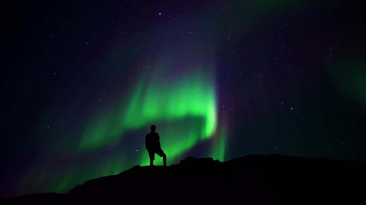 一个人站在悬崖边看着夜空和北极光。视频素材