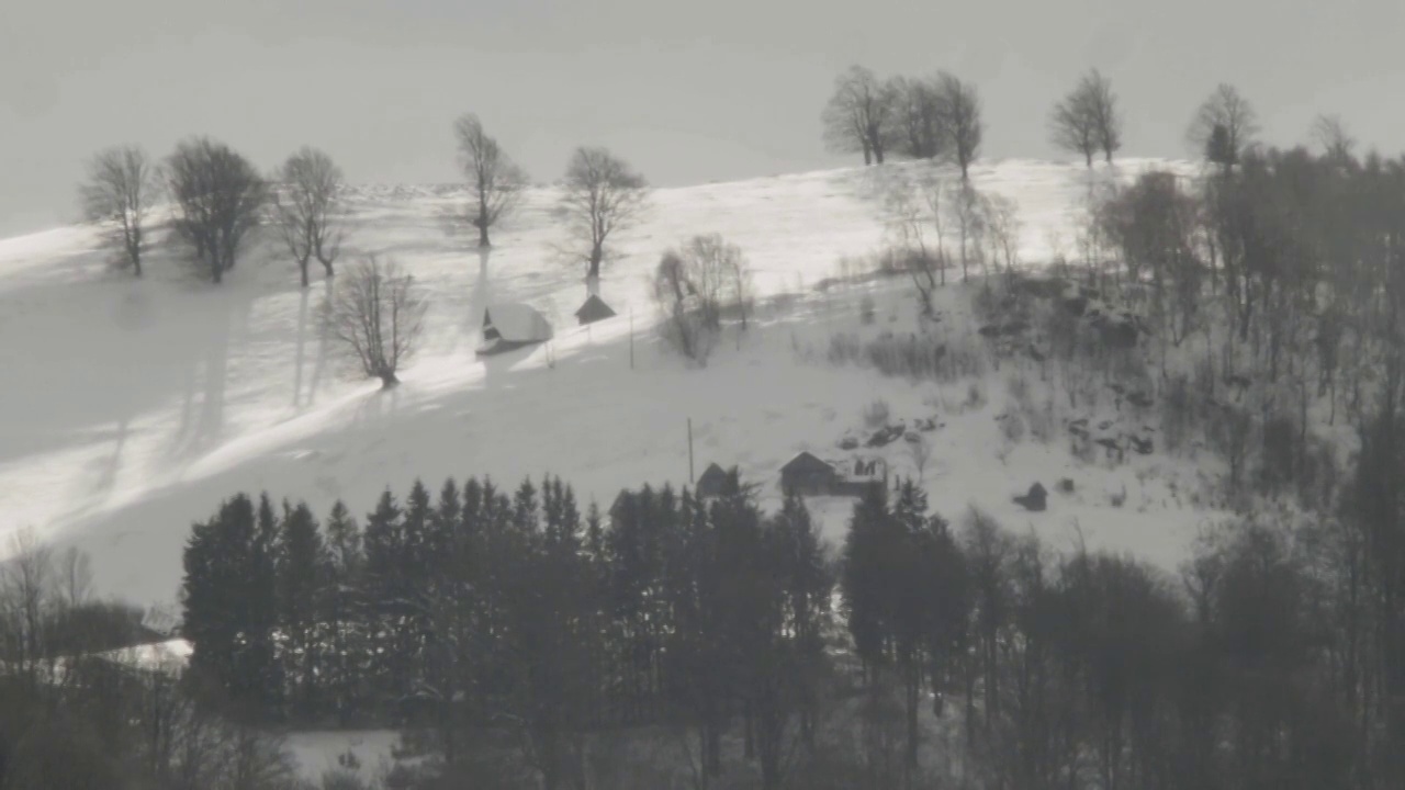 被遗弃的小村庄坐落在积雪覆盖的陡峭山顶上，附近是一片光秃秃的森林，透过稀薄的空气可以看到它扭曲的形象视频素材