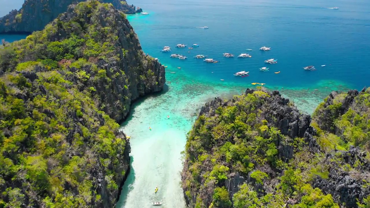 大泻湖，El Nido，巴拉望，菲律宾。无人机在入口浅水上方的石灰岩悬崖之间飞行。跳岛游A船的托里特班卡船在外面等候视频素材