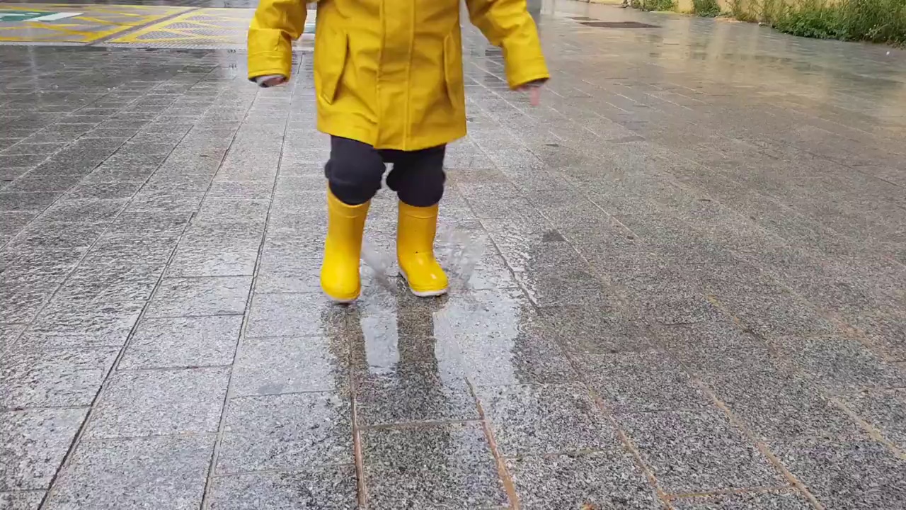 一个孩子穿着雨衣和靴子在水坑里玩耍的剖视图。视频素材