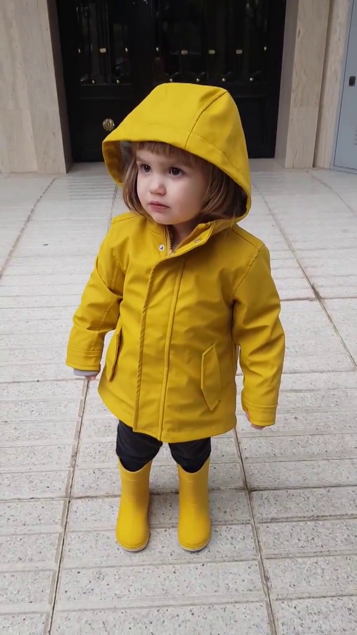 从上面看到三岁的孩子穿着雨衣和雨靴在外面玩耍。视频素材