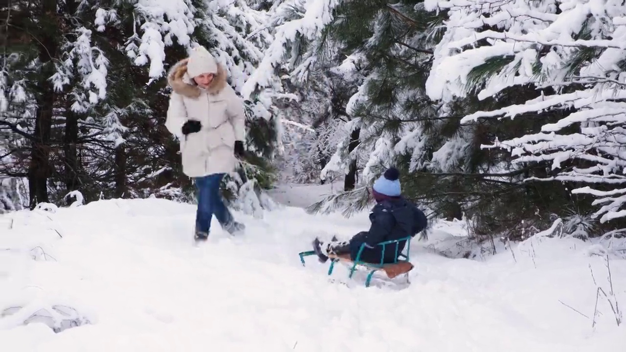 冬天，一位母亲在滑雪胜地的白雪覆盖的森林里拉着她的儿子视频素材