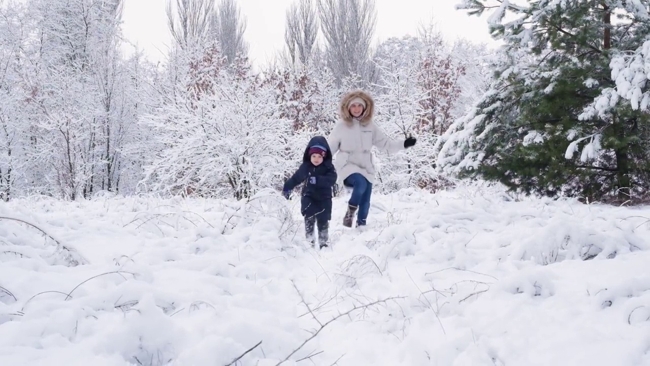 妈妈和儿子在冰雪覆盖的冬季森林里奔跑，快乐的父母和家庭度假，慢镜头视频素材