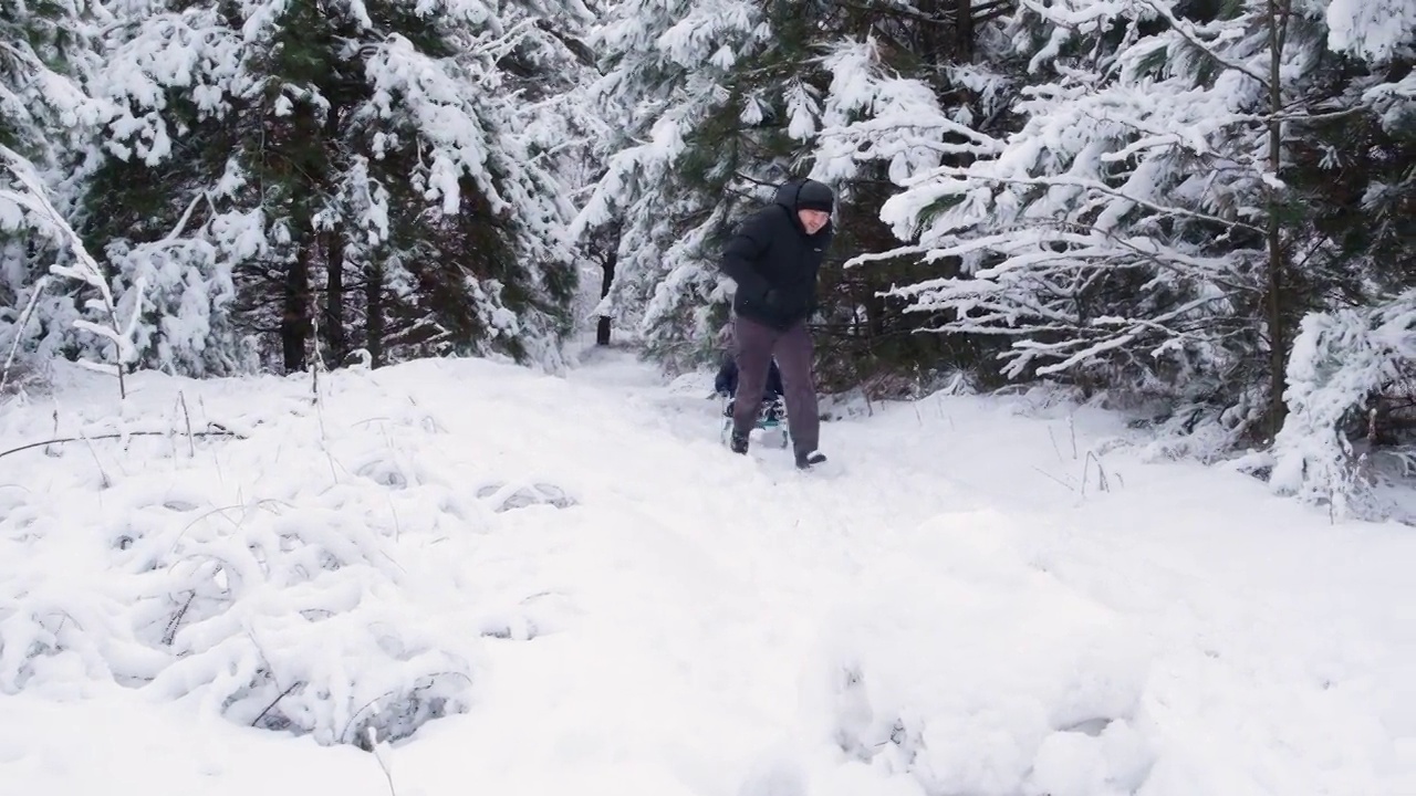 在冰雪覆盖的冬季森林里，爸爸拉着他的儿子在滑雪胜地滑雪，慢镜头拍摄。视频素材