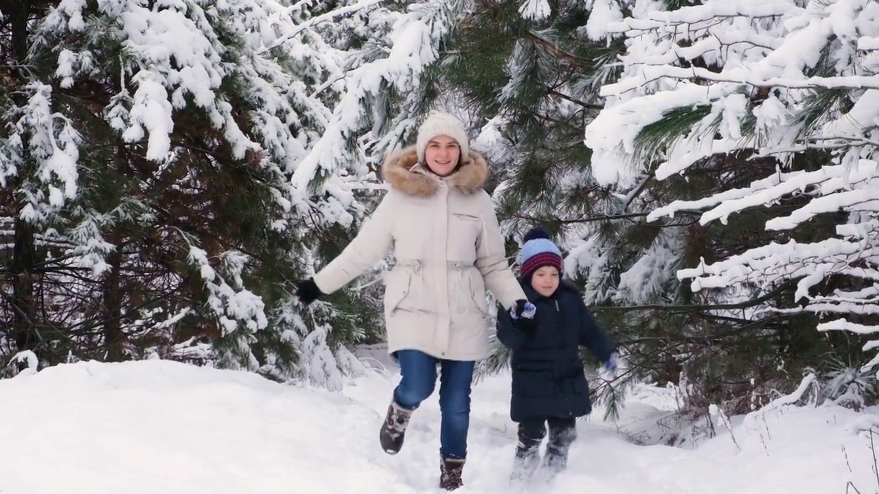 妈妈和儿子在冰雪覆盖的冬季森林里奔跑，快乐的父母和家庭度假，慢镜头视频素材