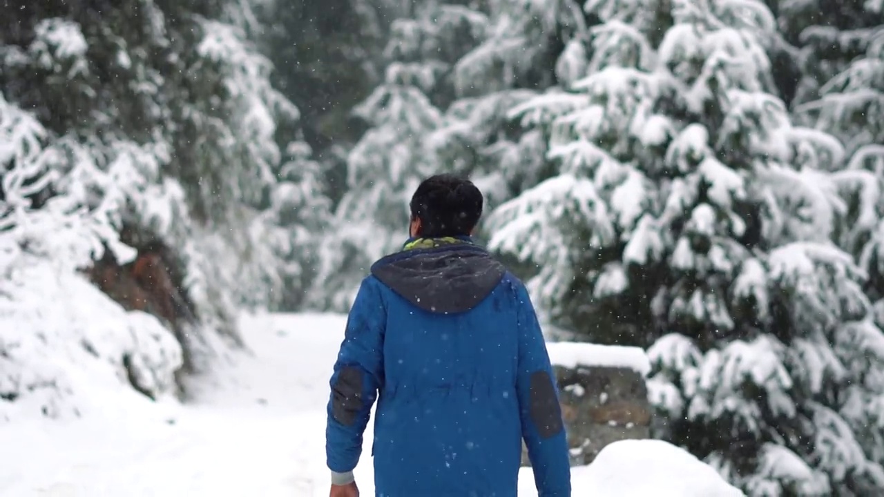 印度喜马偕尔邦马纳里山，一名印度男子行走在积雪覆盖的道路上的慢动作肖像。一个人在冬天下雪的时候走在雪地上视频素材