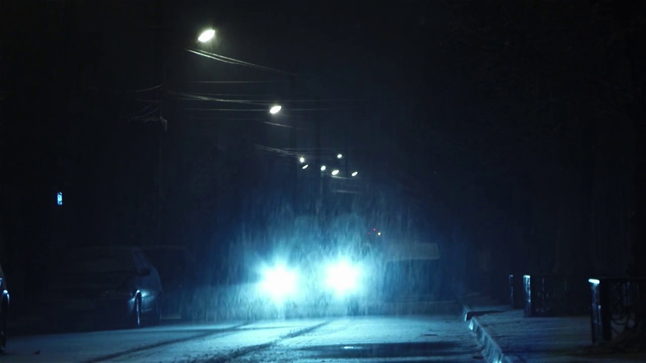 车灯开在铺有路面的街道上，外面正在下雪，虽然雪花很小视频素材