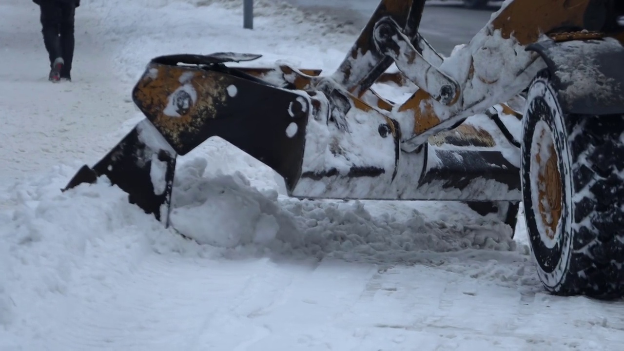 挖掘机，一辆汽车在清理城市街道上的积雪视频下载