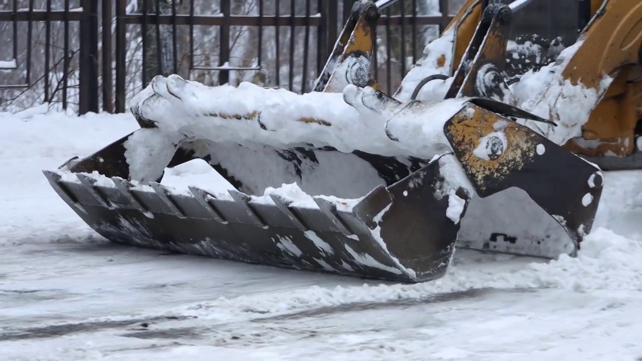 挖掘机，一辆汽车在清理城市街道上的积雪视频下载