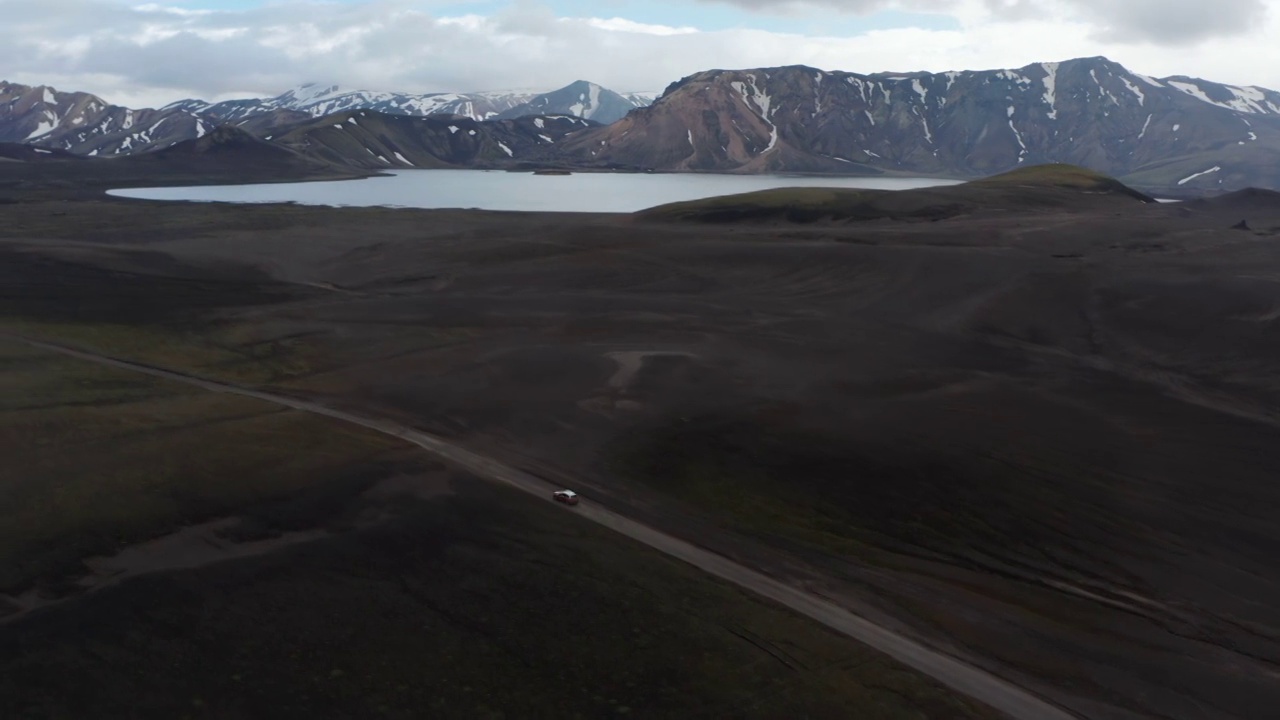 俯视图汽车驾驶沙漠黑色火山地形加速冰岛高地。空中无人机的惊人的冰岛乡村与雪山峰和火山黑沙全景视频素材