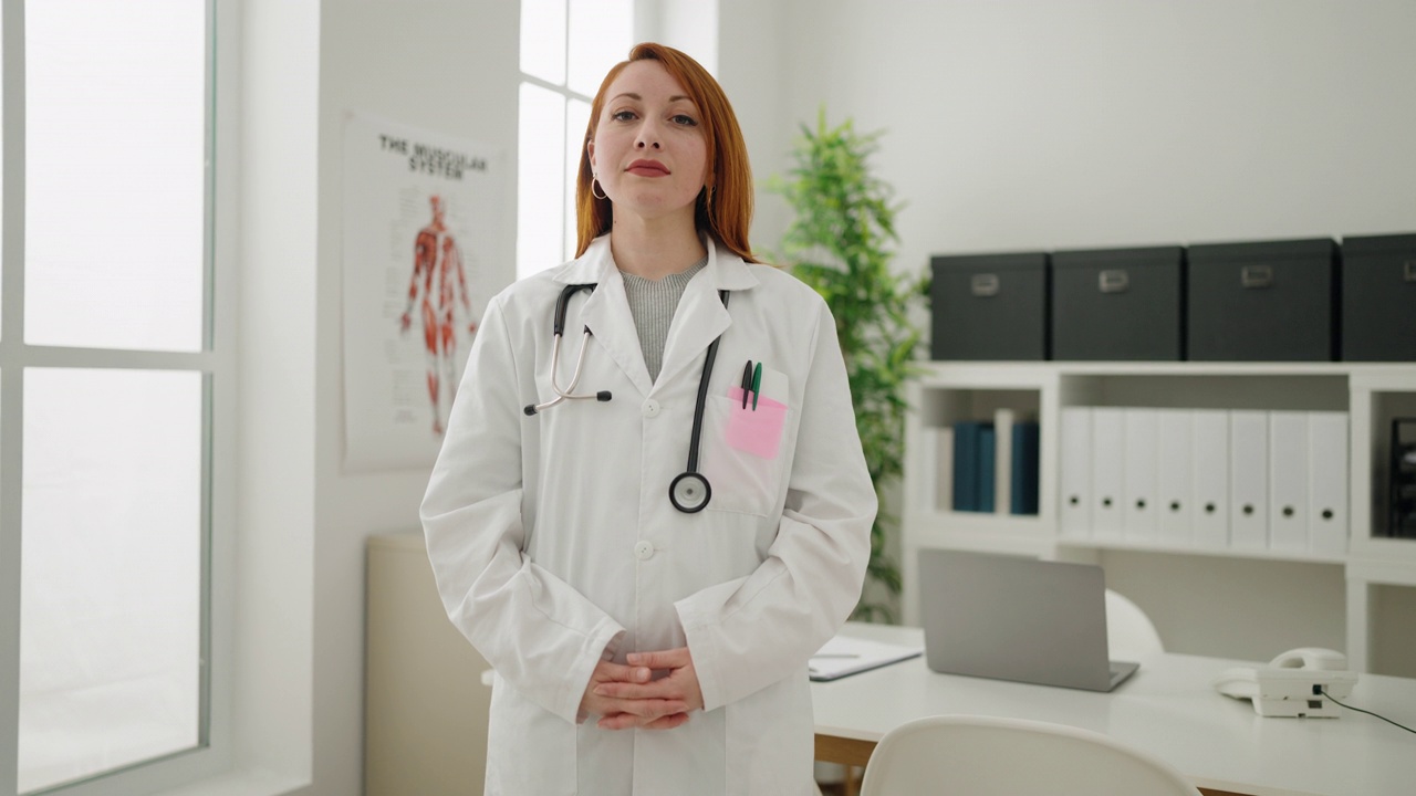 年轻的红发女子穿着医生制服在诊所用手做心脏标志视频素材