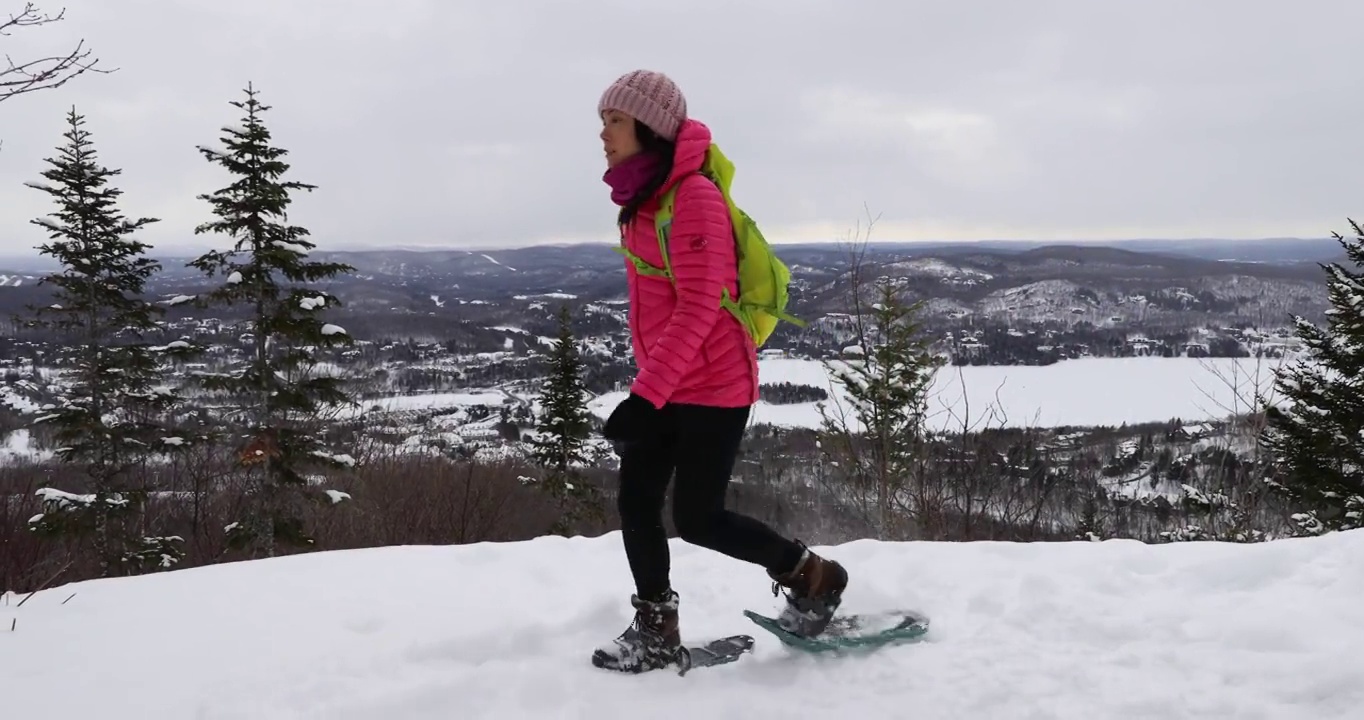 穿雪鞋的妇女在冬季森林徒步旅行在田园诗般的冬季景观。人们穿着雪鞋在雪地里徒步旅行，过着积极的户外生活。加拿大魁北克省劳伦提斯的特伦布兰特山。视频素材