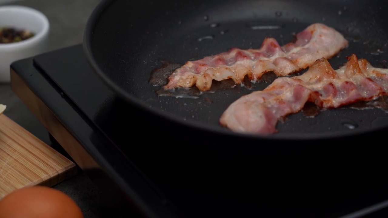 培根煎。肉在热煎锅里咝咝作响。烹饪早餐视频素材