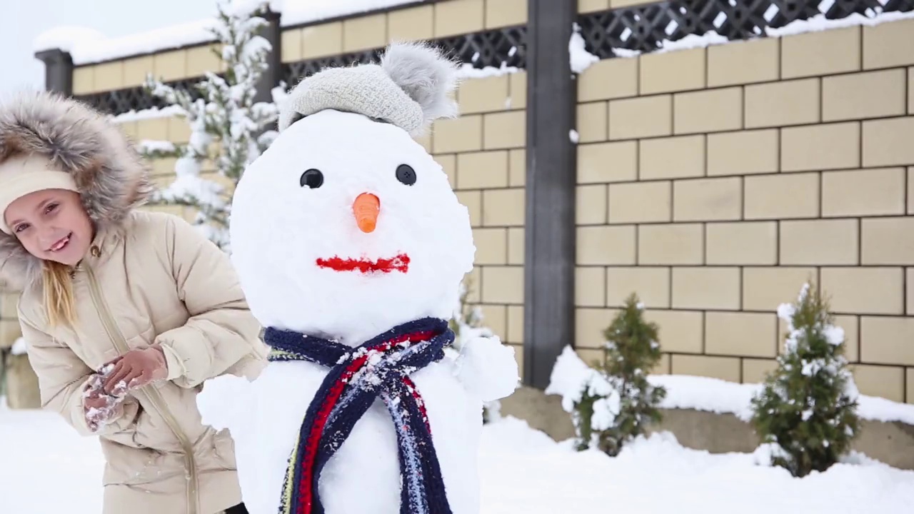 女孩躲在雪人后面笑了。冬季的一场比赛。视频素材