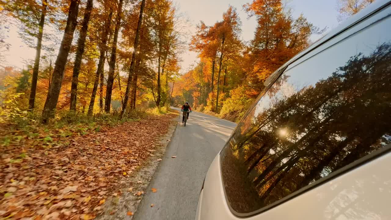 在秋天的一个晴朗的日子里，一名山地自行车手在山路上跟在一辆汽车后面视频素材