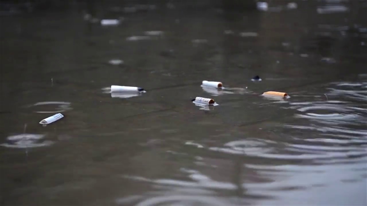 雨点落在一个水坑里，其中丢弃了更多的烟头视频素材