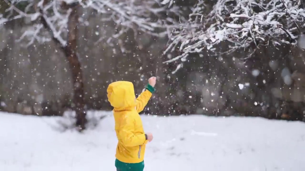 穿着黄色冬衣的滑稽小男孩在下雪时行走。儿童冬季户外活动。视频素材