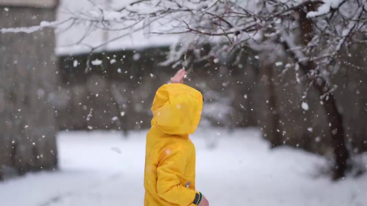 穿着黄色冬衣的滑稽小男孩在下雪时行走。儿童冬季户外活动。视频素材