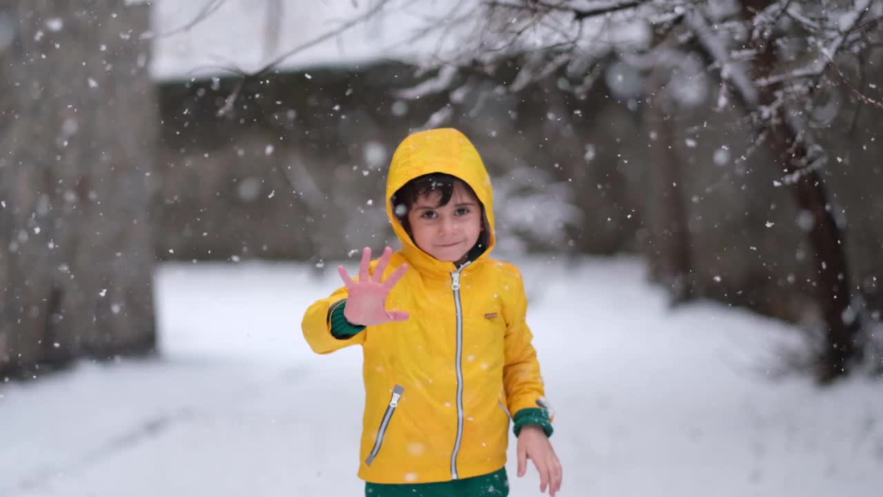 穿着黄色冬衣的滑稽小男孩在下雪时行走。儿童冬季户外活动。视频素材