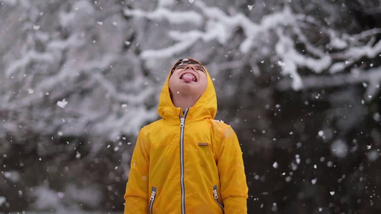 穿着黄色冬衣的滑稽小男孩在下雪时行走。儿童冬季户外活动。视频素材