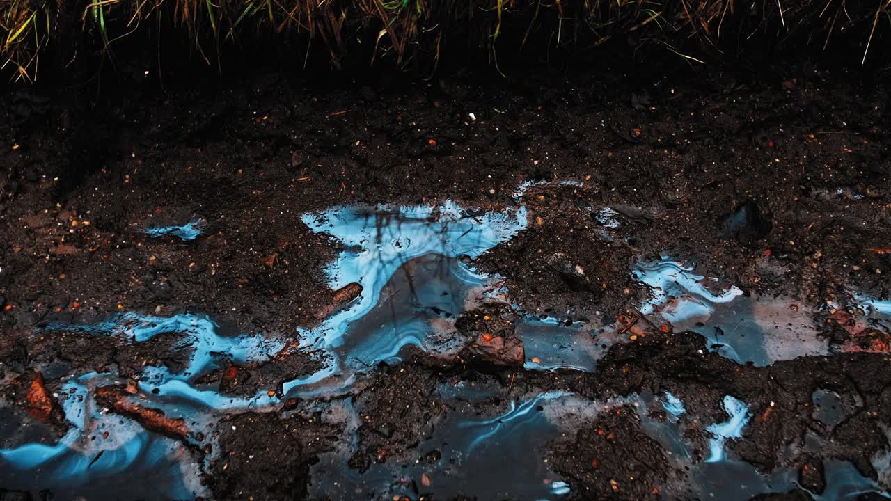 在泥泞的地面和道路上的雨水坑表面，可见有毒工业液体化学污染物的流线污迹视频素材