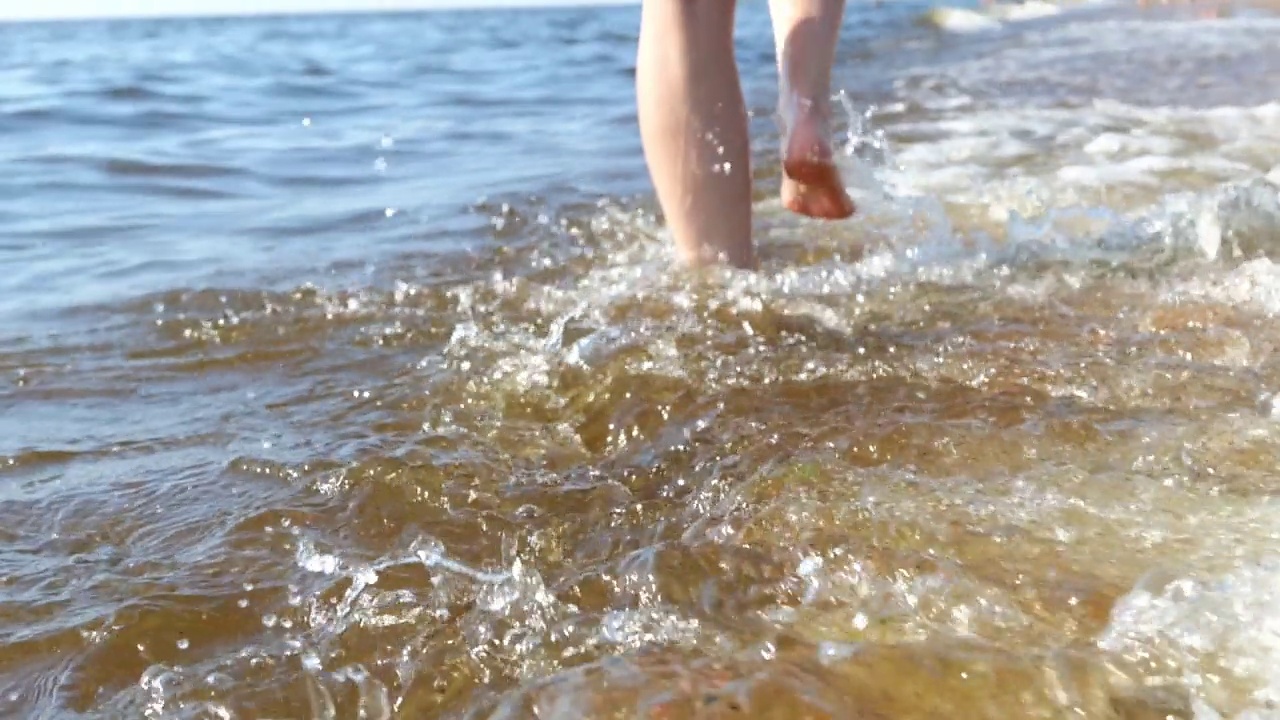 一个模糊的女人的双腿在海边行走的特写，海浪的边缘在她们的脚下轻轻起泡视频素材