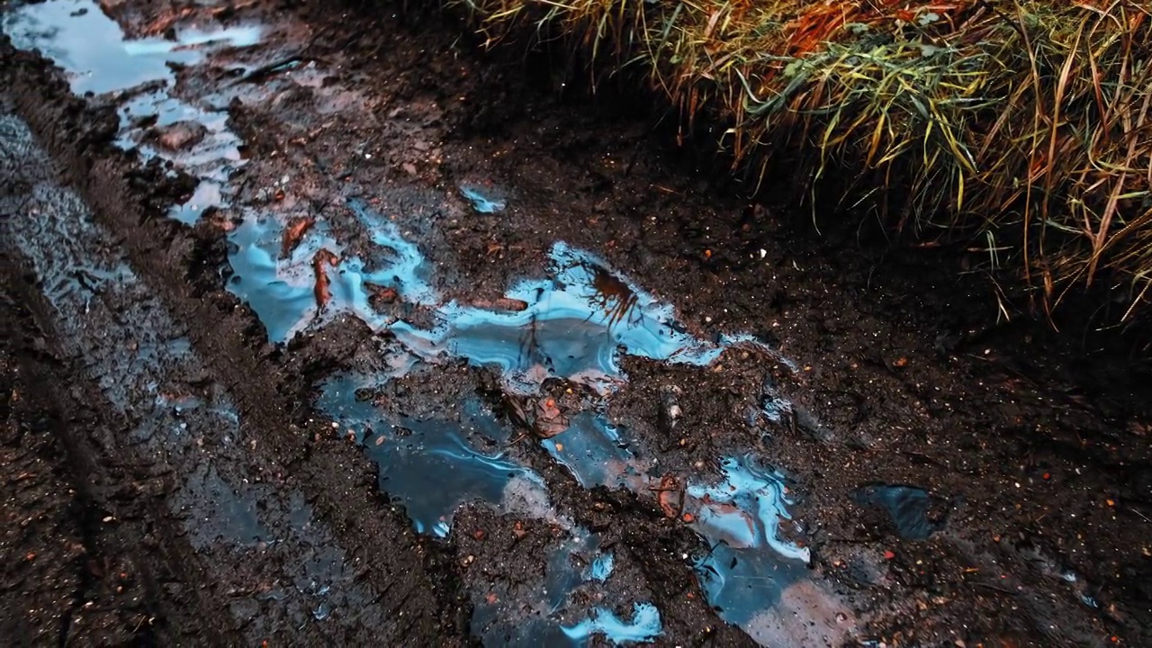 在泥泞的地面和道路上的雨水坑表面，可见有毒工业液体化学污染物的流线污迹视频素材