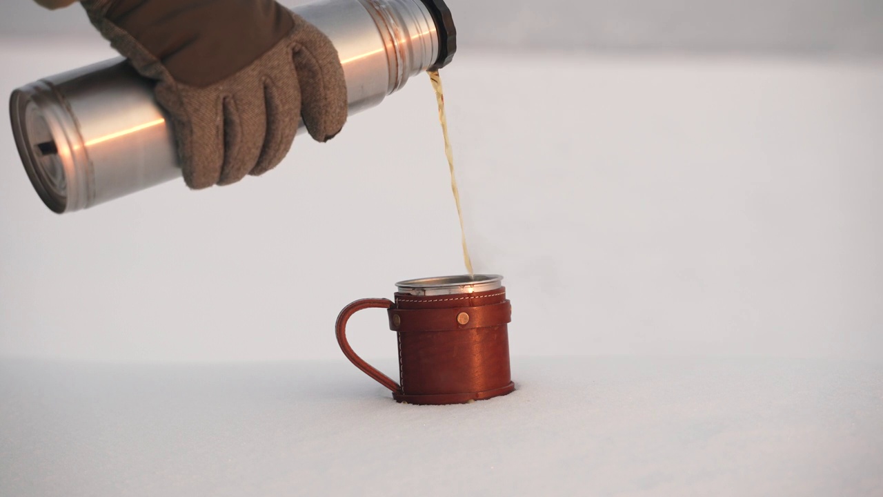 在白雪的衬托下，热茶被倒入一个钢杯中。视频素材