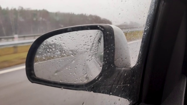 下雨时观看汽车侧镜。汽车侧面的雨滴。在阴雨天旅行。视频素材