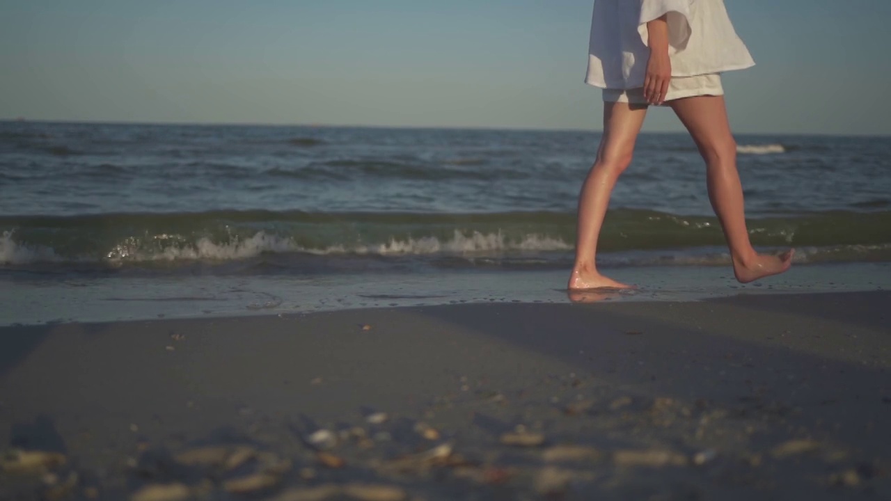 瘦长腿的女孩走在海边的波浪上。夏日沙滩上美丽的蓝绿色海水。放松和旅游，度假的概念。温暖的阳光明媚的天气。缓慢的运动。视频素材