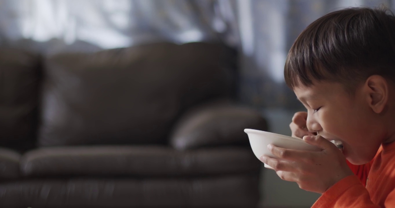 穿着橙色衬衫的男孩正用勺子吃得津津有味。视频素材